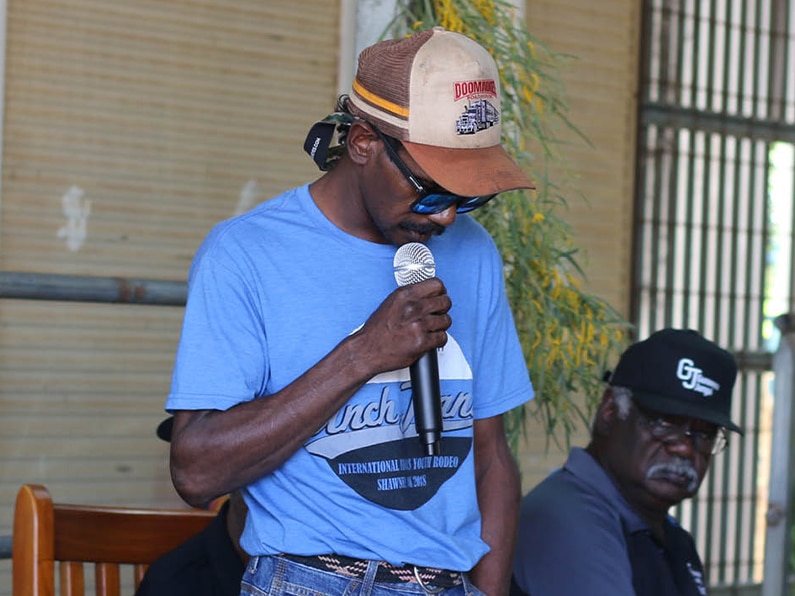 Jungai summit | gunawuna jungai | gunawuna jungai Man in a blue t shirt and brown cap holding a microphone performing at an outdoor event