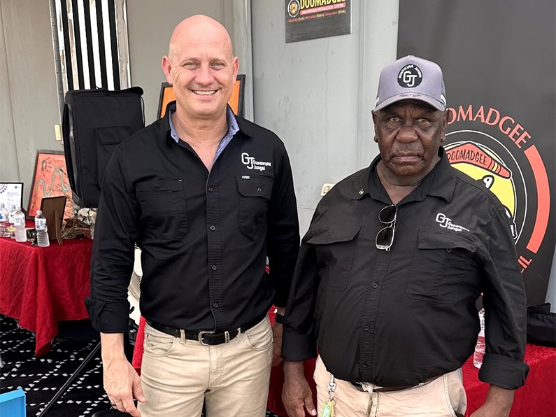 Two men in black gt uniforms stand at an event booth with a red tablecloth behind them